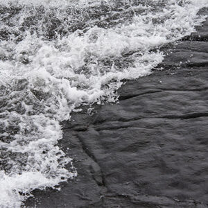 Close-up wave progression covering dark shoreline rock in a three-part lake superior basalt triptych print set.